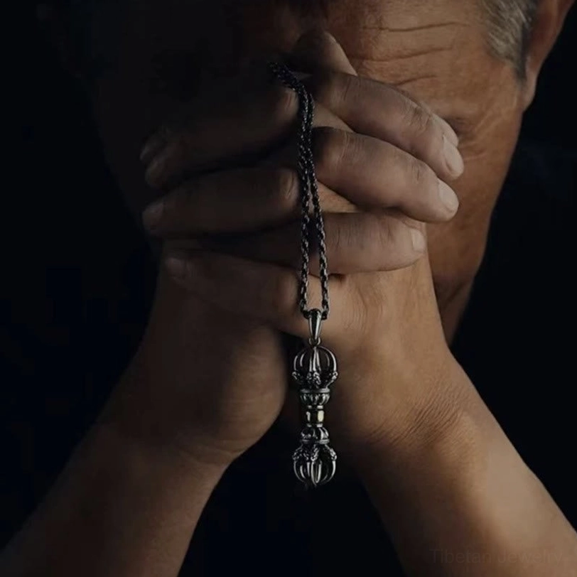 Lifestyle photograph of Tibetan Dorje Vajra necklace worn and held in hands under moody lighting, showing daily wearable pendant size