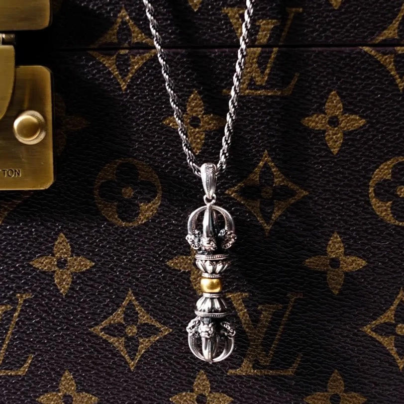Tibetan Dorje Vajra pendant and wheat chain necklace laid flat on luxury monogram leather with vintage silver and gold finish