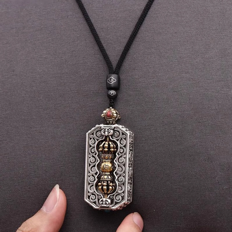 Tibetan dorje vajra necklace pendant with black wax rope displayed on gray fabric background showing silver-gold dual tone and filigree details