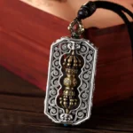 Tibetan Dorje Vajra Om Mani Padme Hum rotatable pendant necklace with filigree engravings and inlaid red gemstone on wooden background