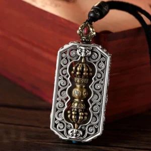 Tibetan Dorje Vajra Om Mani Padme Hum rotatable pendant necklace with filigree engravings and inlaid red gemstone on wooden background