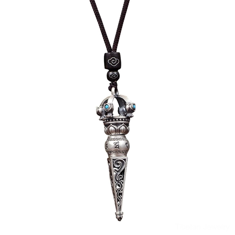 Macro close-up of Tibetan Dorje Vajra pendant showing detailed scroll carvings, Sanskrit mantra engravings, and matte silver finish with turquoise inlays