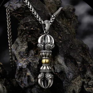 Tibetan Dorje Vajra pendant necklace in two-tone silver and gold, displayed on dark textured rock surface showing intricate carved details