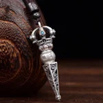 Tibetan Dorje Vajra rotating pendant necklace with turquoise inlays and engraved Om Mani Padme Hum mantra, left front oblique view showing intricate scroll carvings and copper finish