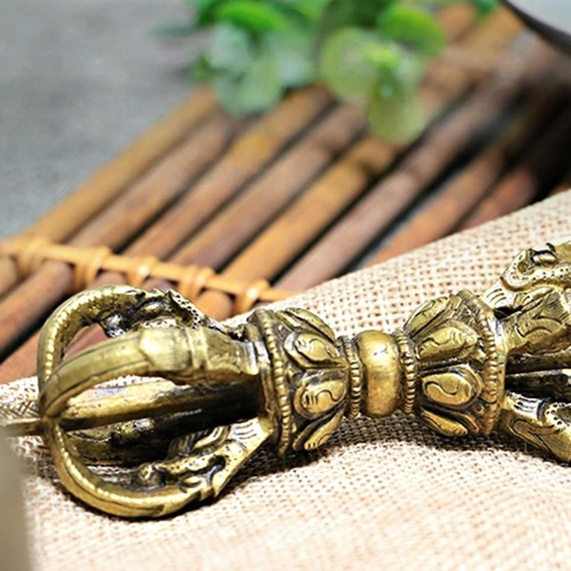 Vajra dorje top-down view displaying polished bronze copper finish with intricate embossed religious design, surrounded by burlap and bamboo mat