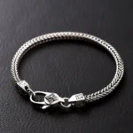 Tibetan Double Dorje Vajra Bracelet - Flat lay with silver braided wheat chain design and carved clasp on dark leather