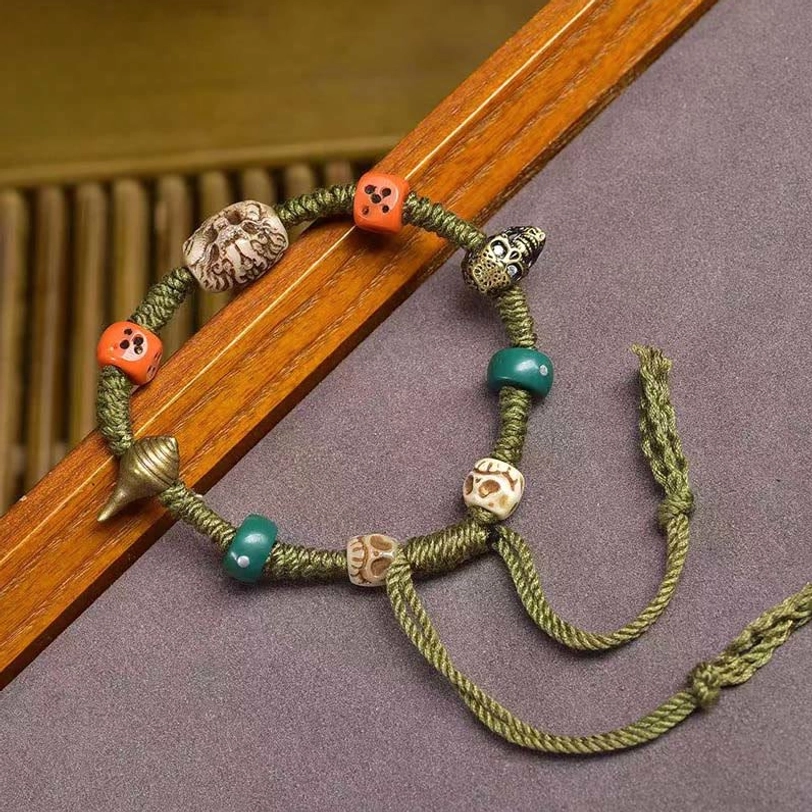 Green woven cord bracelet side view showing olive rope texture, mixed ethnic beads, and adjustable tassel on wooden handrail