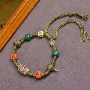 Tibetan dragon dice bracelet with green rope, carved dragon beads, orange dice beads, and metal charms displayed on dark textile