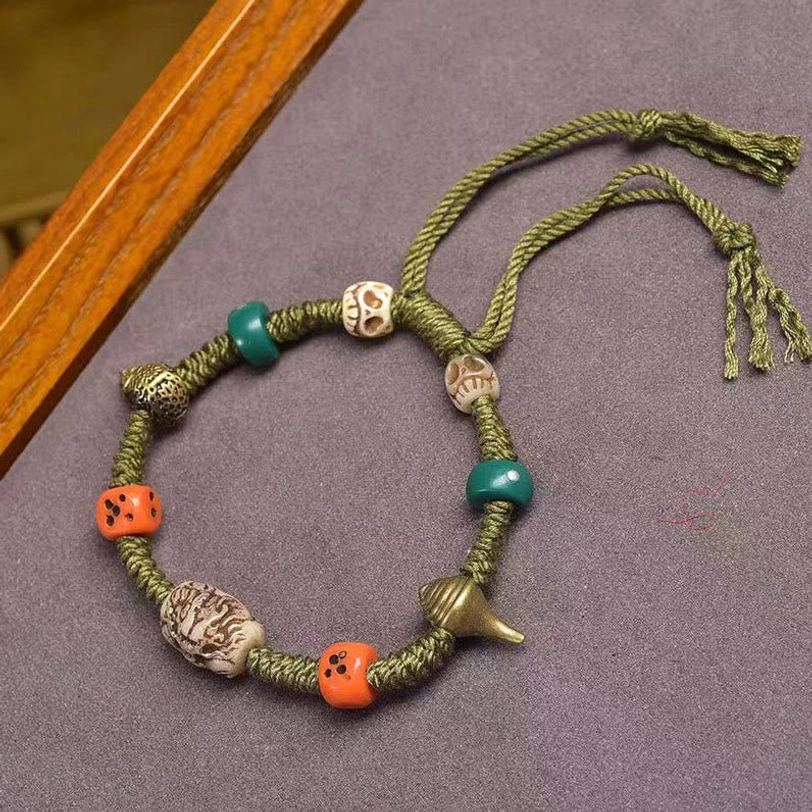 Tibetan dragon dice bracelet with green rope, carved dragon beads, orange dice beads, and metal charms displayed on dark textile