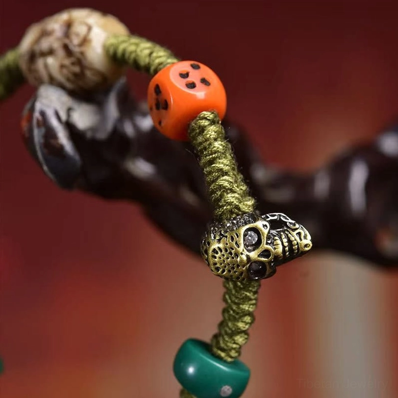 Macro view of handmade bracelet featuring carved skull beads, orange dice, metal skull charm, and green stone bead on wooden background