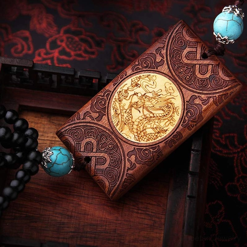 Side angle view of Tibetan dragon hanging showing intricate carvings, golden dragon inlay, and black beaded chain against dark wooden background