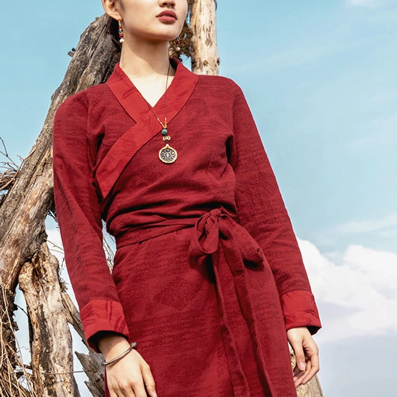 Upper body detail of burgundy Tibetan wrap dress showing cuffed long sleeves, woven texture, and pendant necklace accessory