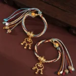 Handcrafted Dunhuang deer auspicious cloud healing bracelet with gold bell lock on dark wood surface, multicolor braided cord detail
