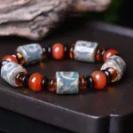 Tibetan Three-Eye Dzi Bead Agate Bracelet - overhead flat lay view on dark wooden tray showing aged etched patterns, red agate beads, and dark glass spacers