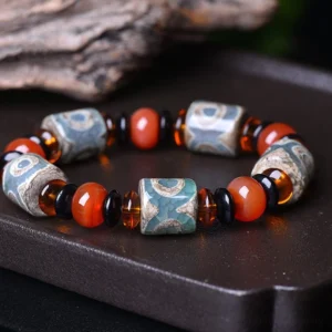 Tibetan Three-Eye Dzi Bead Agate Bracelet - overhead flat lay view on dark wooden tray showing aged etched patterns, red agate beads, and dark glass spacers