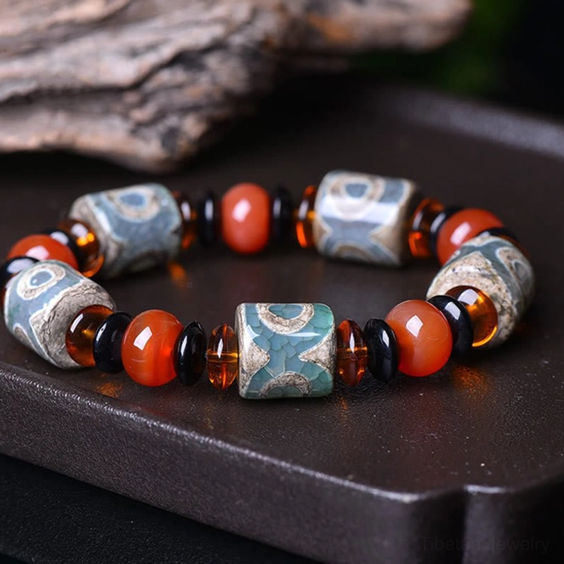 Tibetan Three-Eye Dzi Bead Agate Bracelet - overhead flat lay view on dark wooden tray showing aged etched patterns, red agate beads, and dark glass spacers