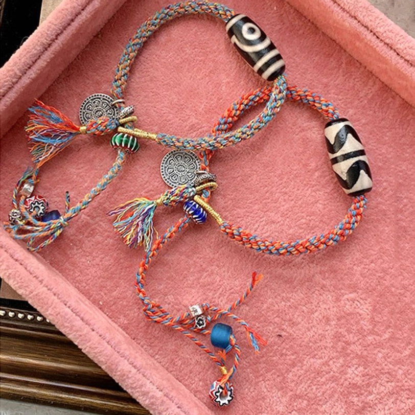 Blue Tibetan Nine-Eye Dzi bead bracelet with sterling silver charm and colorful tassel on pink velvet background