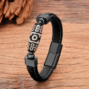 Tibetan Nine-Eye Dzi Bead leather bracelet with magnetic buckle, black leather strap with geometric patterned bead, three-quarter view on wooden background