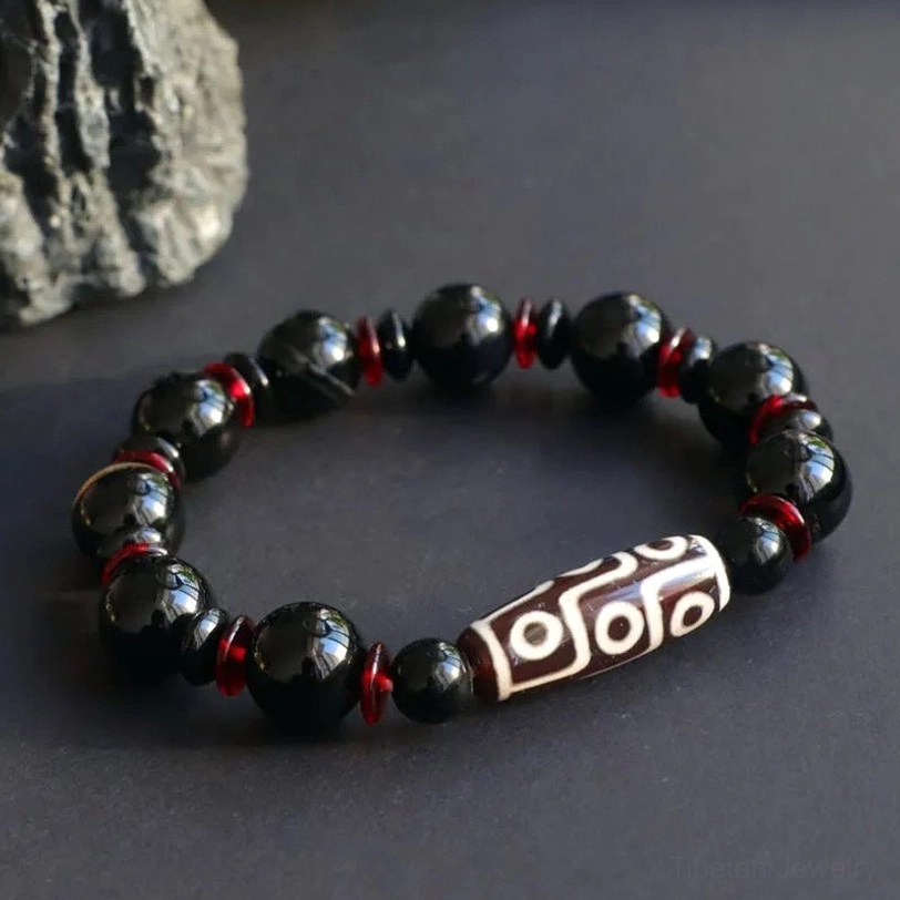 Nine-Eye Dzi Bead Tibetan bracelet on display with rough stone backdrop, highlighting the contrast between black onyx beads and the central white nine-eye focal bead