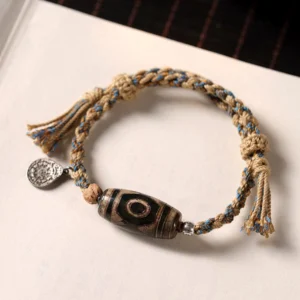 Tibetan Dzi bead wealth protection bracelet featuring two-eye stone bead, round metal charm, and wooden spacer beads on white paper