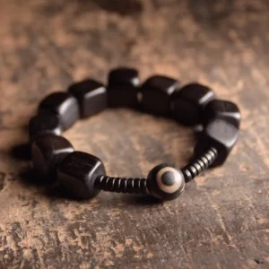 Tibetan ebony wood nine-eye dzi bead bracelet overhead view with square black wooden beads and hand-painted dzi accent on rustic wooden surface