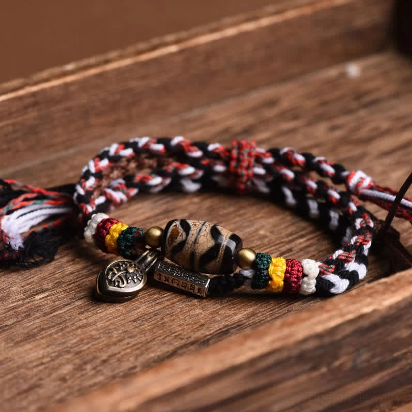 Overhead view of double-wrap Tibetan Dzi bead bracelet with striped woven rope, patterned Dzi bead, and decorative colored spacer beads