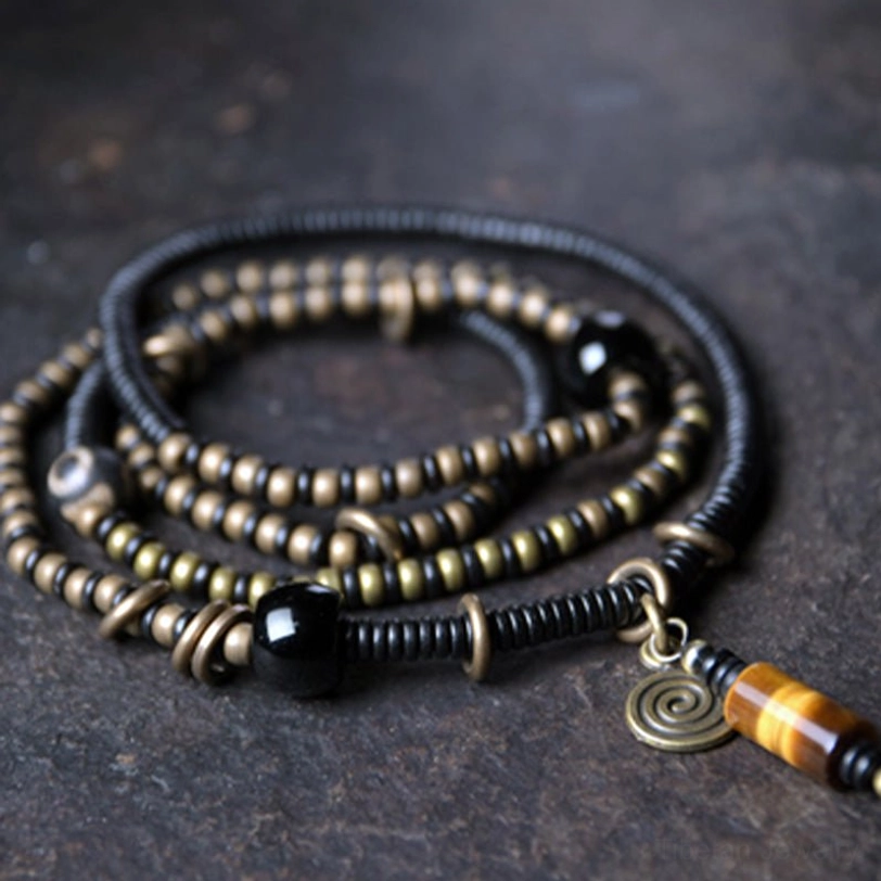 Tibetan ebony wood Dzi bead copper bracelet necklace set with tiger eye pendant and spiral charm, flat lay on dark stone surface