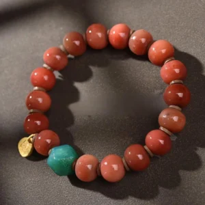Tibetan beaded bracelet featuring earthy red camel bone beads, turquoise accent stone, and gold metal charm in minimalist flat lay style