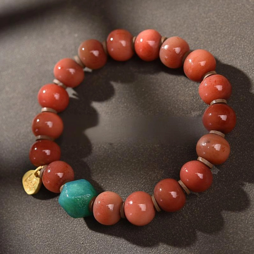 Tibetan beaded bracelet featuring earthy red camel bone beads, turquoise accent stone, and gold metal charm in minimalist flat lay style
