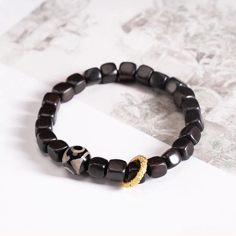Single tibetan dzi bead ebony wood bracelet flat lay on vintage paper with three-eye symbol