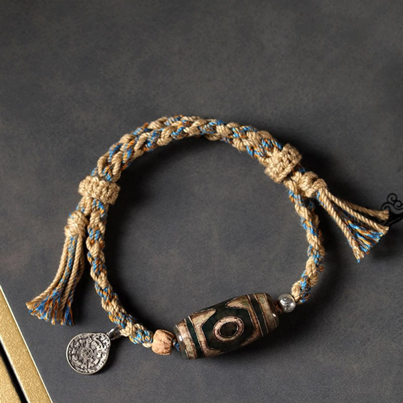 Hand-woven Tibetan Dzi bead bracelet with khaki-blue mixed cord, aged protective amulet bead, and engraved metal charm on dark background