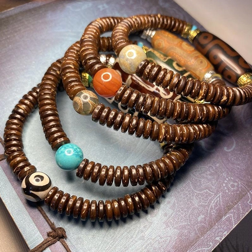 Stacked Tibetan dzi bead bracelets featuring multiple designs including yin-yang bead, turquoise, red agate, and brown disc beads on vintage paper