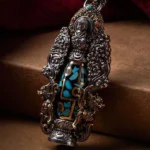 Tibetan nine-eye dzi bead Buddha turquoise pendant with intricate two-tone metalwork and carved floral patterns on wooden surface
