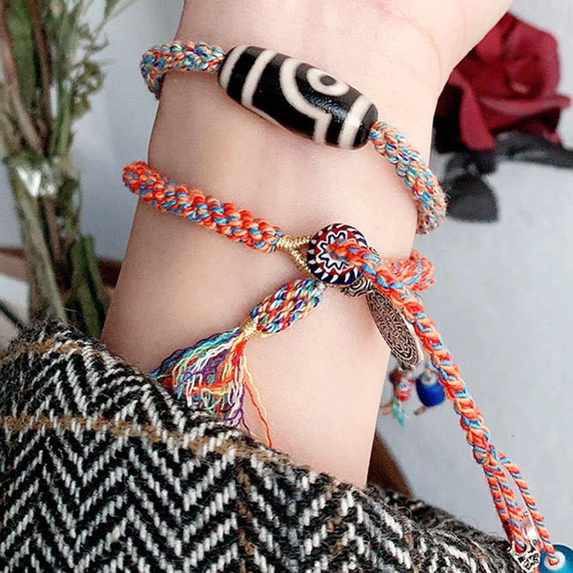 Two Tibetan Dzi bead protection bracelets worn together on wrist with silver charms and colorful tassels