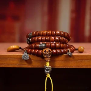 Close-up eye-level view of Tibetan dzi bead mala on wooden display shelf featuring reddish-brown beads with silver metal ornaments