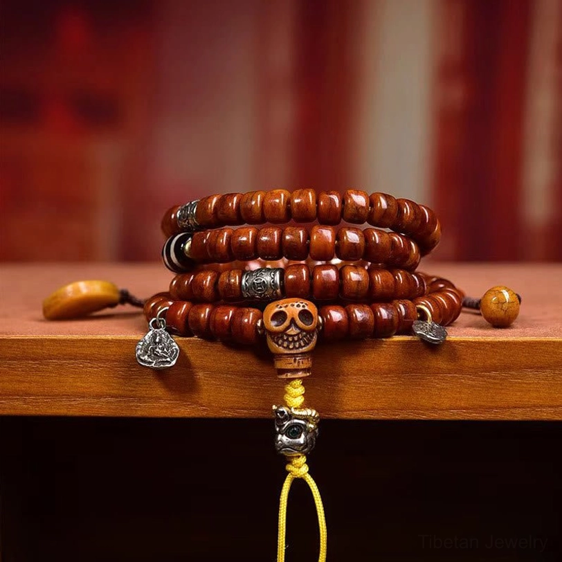 Close-up eye-level view of Tibetan dzi bead mala on wooden display shelf featuring reddish-brown beads with silver metal ornaments