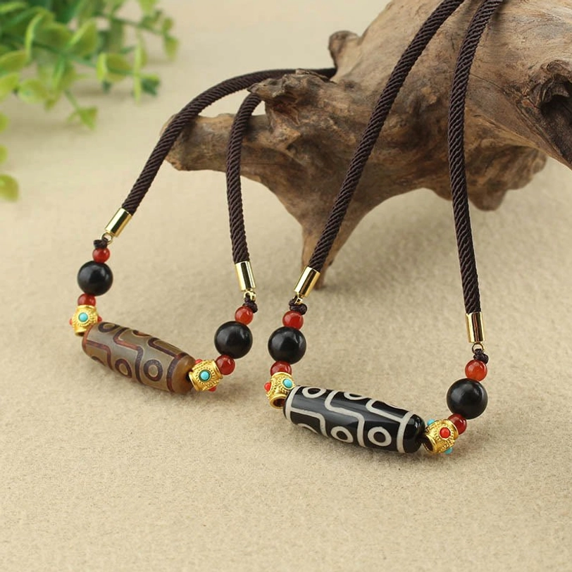 Two Tibetan dzi bead necklaces brown and black-white styles displayed on wooden stand with green plants