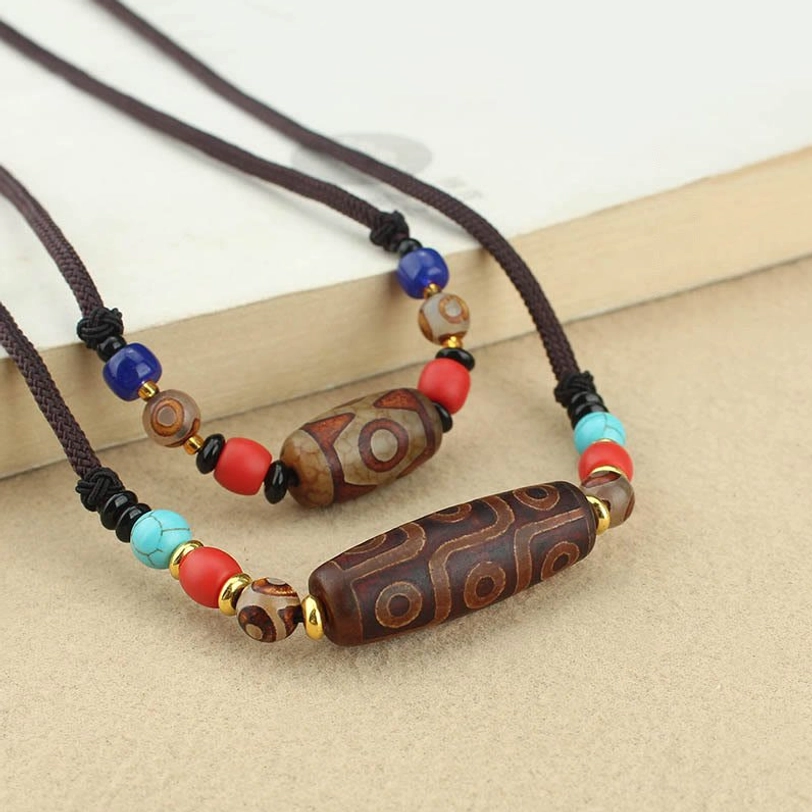 Tibetan dzi bead necklaces flat lay overhead view featuring nine-eye and three-eye dzi beads on brown woven cord with colorful gemstone accents on wooden desktop