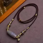 Nine-eye dzi bead necklace with Om Mani Padme Hum charm flat lay on wooden surface showing full pendant design