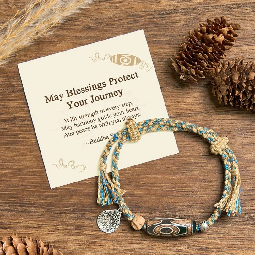 Nine-eye Dzi bead bracelet overhead view with braided rope, copper charm, and pine cone styling on wooden table with blessing card