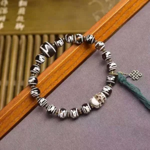 Hand-painted Tibetan Dzi beads with intricate patterns and green tassel detail on bamboo blind background