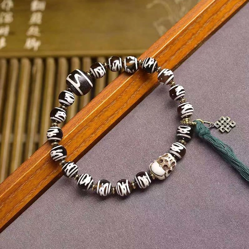 Hand-painted Tibetan Dzi beads with intricate patterns and green tassel detail on bamboo blind background