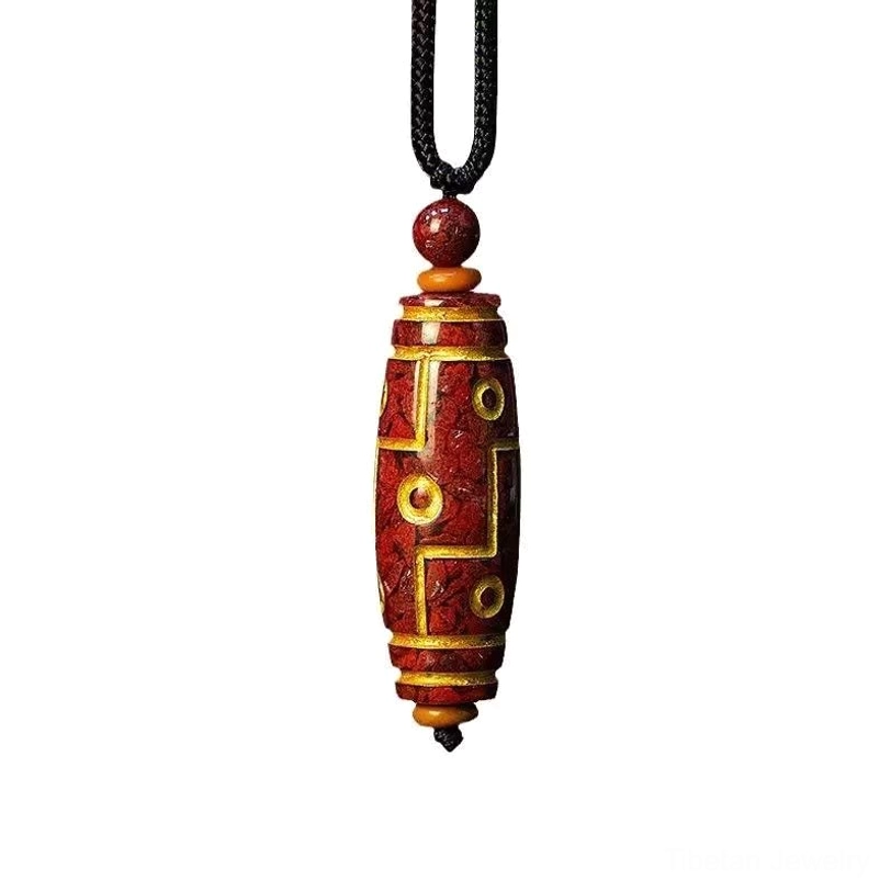 Nine-eye Tibetan dzi bead pendant with reddish-brown cinnabar body and gold decorative motifs on plain white background