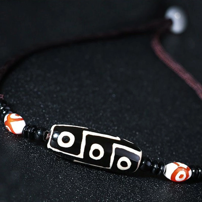 Single Tibetan three-eye dzi bead pendant necklace with black cord - close-up detail shot on dark fabric background