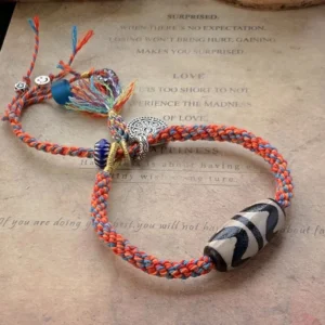 Red Tibetan Nine-Eye Dzi Bead bracelet with 925 sterling silver Om Mani Padme Hum charm on vintage paper background