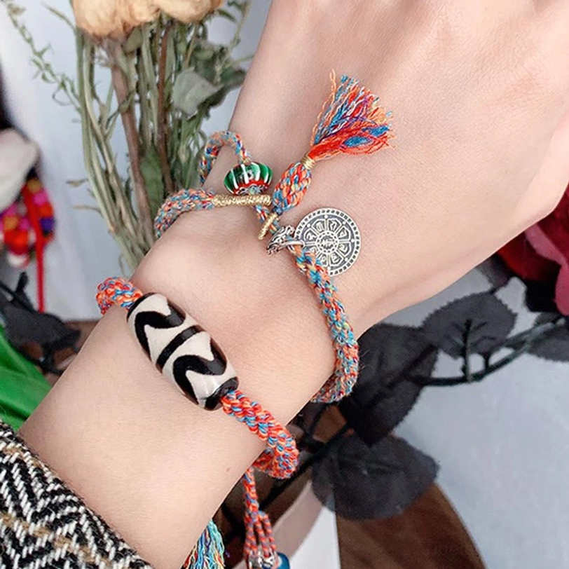 Woman wearing red Tibetan Dzi bead bracelet with silver charm and green accent bead on wrist with indoor plants
