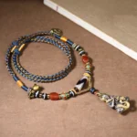 Handmade Tibetan Dzi bead snake Buddha pendant necklace with red agate beads and braided cord, top-down view on light background