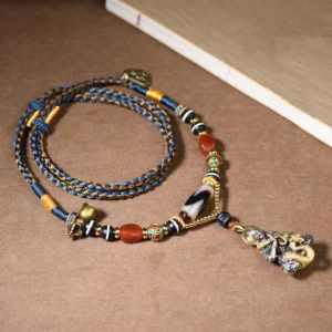 Handmade Tibetan Dzi bead snake Buddha pendant necklace with red agate beads and braided cord, top-down view on light background