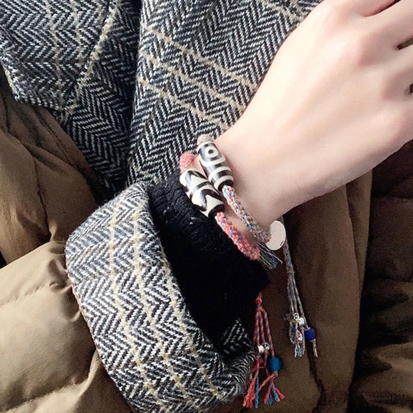 Person wearing striped Tibetan Dzi bead bracelet with silver charm and colorful tassel on wrist, side close-up