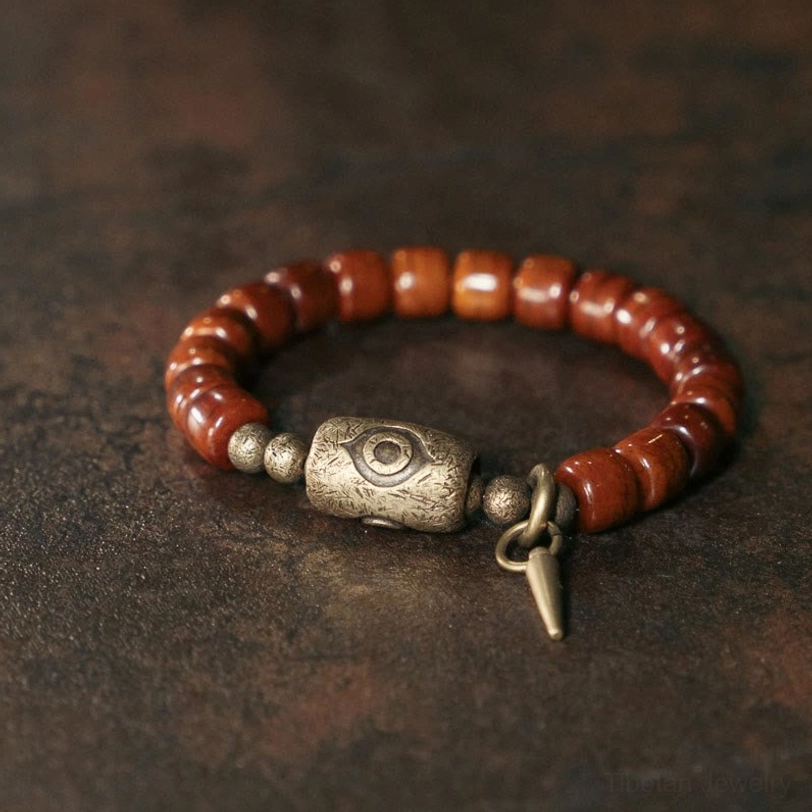 Tibetan bone bead Dzi bracelet with copper eye charm and cone pendant, top-down front view showcasing intricate beadwork and bronze accents
